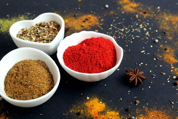 On a black background there are spices in cups.	
