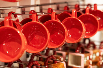 Glossy red ceramic cups hang from hooks in tidy rows; selective focus and warm tones create a bright, modern store display with strong color rhythm.