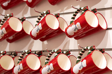 Red ceramic mugs with snowman art hang in neat rows on a wall rack; selective focus, warm light and...