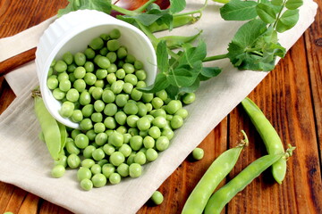 There is a wooden cup with green fresh peas on the wooden table.	