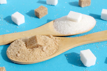 Wooden spoons with white and brown sugar lie on a blue background.