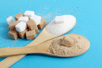Wooden spoons with white and brown sugar lie on a blue background.