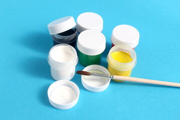 There are jars of gouache paints on a blue background.	