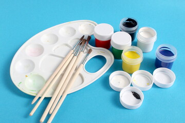 On a blue background lies a white used palette with cans of gouache paint.	