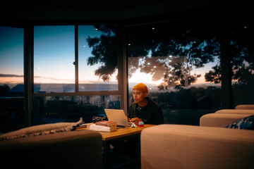 An individual deeply focused on working on their laptop during a beautiful sunset while enjoying a cozy atmosphere