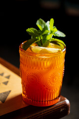 A vibrant drink rests on a wooden table, topped with fresh mint and lemon, inviting relaxation