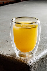 A refreshing amber beverage sits in a clear glass, capturing soft light on a textured surface