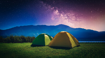 Yellow and green camping tent on grass near mountain river with milky way at night