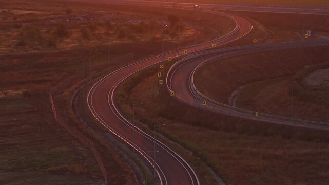 Wide aerial shot a highway interchange at a dramatic sunset or sunrise, with the distant city skyline on the horizon. 4k aerial video with a highway exit or entrance.