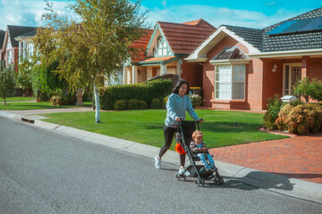 A joyful woman strolls through a vibrant suburb with a child peacefully in a stroller on a sunny day