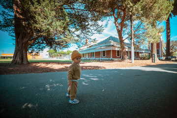 Charming toddler exploring a park with a picturesque house in the background.