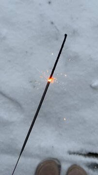 A burning sparkler held in a hand against a snowy background. Vertical winter video with festive mood, cold season atmosphere, minimal and cozy holiday concept.