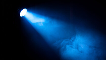 A single blue spotlight beam illuminates smoke or fog against a dark background, creating a dramatic effect
