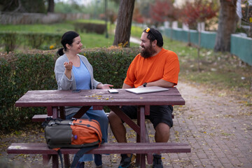 Fototapeta premium Modern freelancers working on laptops in nature. Man and woman working on laptops in public park. Remote work concept with couple using computers outdoors.