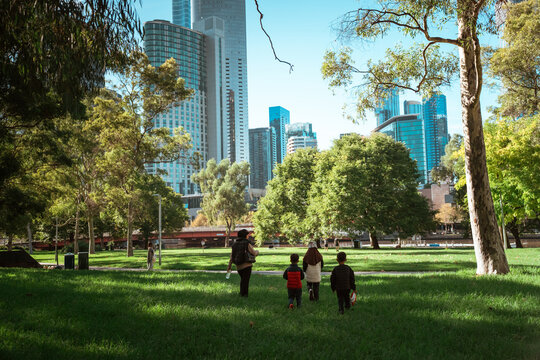 A family joyfully walking in a lush park with a vibrant city skyline backdrop