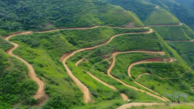 Winding dirt road with many hairpin turns ascending a lush green, steep tropical mountain landscape from an aerial perspective