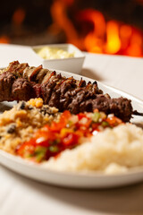Macro close-up of mixed meat skewer with rice, farofa, and chopped peppers and onions.