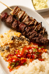 Macro close-up of mixed meat skewer with rice, farofa, and chopped peppers and onions.