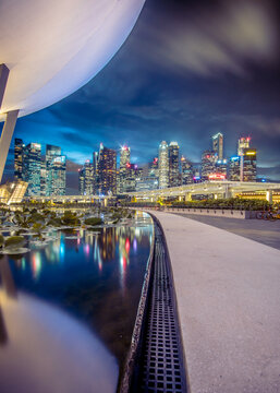 View of gleaming city lights reflecting on tranquil waters beneath the ArtScience Museum, contrasting against the dark night sky, Raffles Place and Marina Boulevard, Singapore, Singapore.