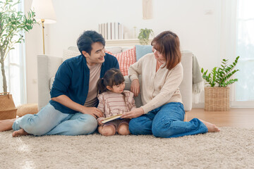 Asian parents and cute daughter sit on a plush, sunny rug, reading a storybook together. Happy family bonding through learning in the cozy living room.