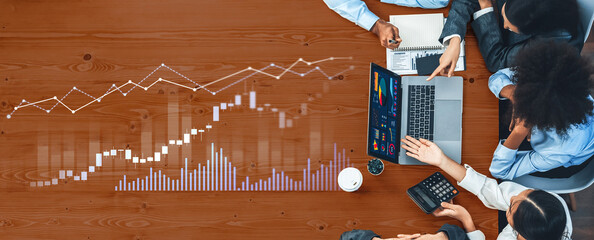 A diverse team collaborates in a business meeting, analyzing stock market data on a laptop. Charts and graphs indicate financial insights for informed decision-making. Scalp
