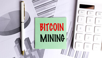 Green card text bitcoin mining on office desk with charts, pen, and calculator, symbolizing cryptocurrency generation