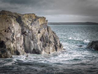 Strong waves crash against the rugged cliff face on the coast. The sea pounds against the rocks.