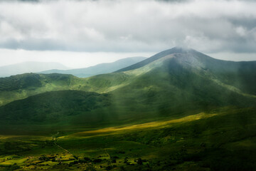 the green landscape of Coomloughra. Sunlight shines through the cloudy sky onto the mountains in Ireland.