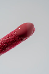 A clean lip gloss applicator tip is coated in a thick layer of rich, red gloss. The glossy, wet-look texture and vibrant color highlight the product's high-shine, reflective finish.