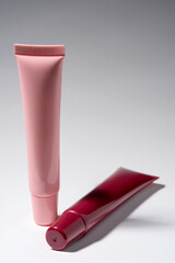 Soft Pink Cosmetic Tube Standing Upright Beside Red Lipstick Tube on Gray Studio Background Backdrop