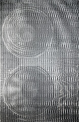 Superficie oscura con patr&oacute;n de rejilla y dos formas circulares superpuestas visibles por sombreado sutil.profundidad y resonancia, simbolizando estructura, silencio y presencia ac&uacute;stica abstracta.