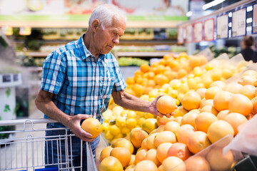 Mature senor examines oranges in fruit section of supermarket