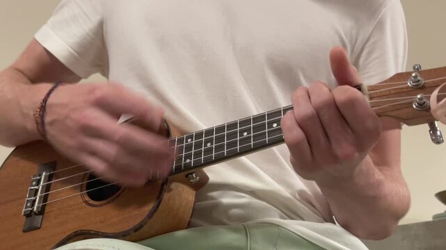 Close up Ukulele or uke string instrument video popular on Hawaii islands. Teenager boy playing nylon strings during music lessons in living room. Musical education and art people concept 4K footage