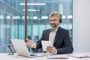 Mature businessman wearing a headset and suit engaging in a virtual online video conference...