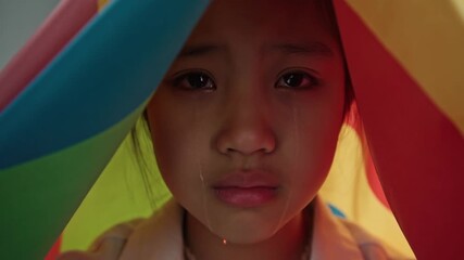 A sad girl with tears is crying. The girl is under a colorful sheet, looking down, expressing sadness and pain. Stock Video