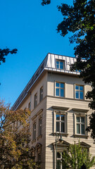 Corner side of a three-story house with windows against a blue sky and trees around