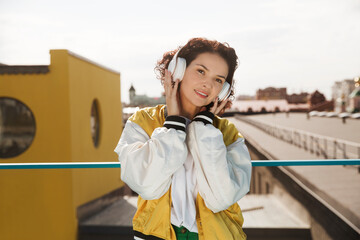 smiling middle aged woman with headphoneson  enjoying the view of the city from a high vantage point. Audio guide. Mindfulness and feel-good moments. Audio healing. 