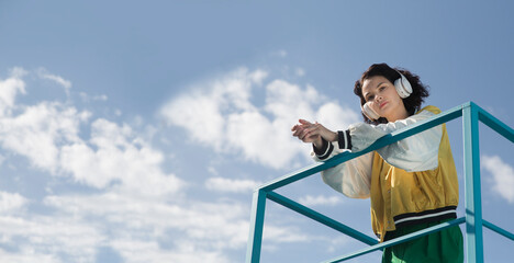 smiling middle aged woman with headphoneson  enjoying the view of the city from a high vantage point. Audio guide. Mindfulness and feel-good moments. Audio healing. 