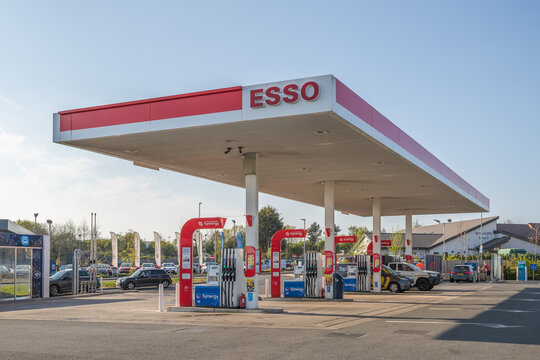A modern Esso petrol station with Synergy fuel pumps under a large canopy on a sunny day, with several cars refuelling in Bristol, UK