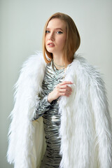 A beautiful woman in a white fur coat is sitting on a leather sofa. She has long blonde hair that hangs loose and has beautiful earrings in her ears.