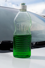 Plastic bottle with green liquid and white cap placed on car hood.