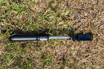 Black and silver selfie stick with telescopic arm placed on dry grass