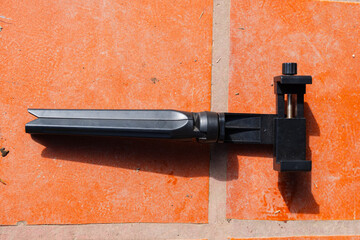Folded black tripod with adjustable phone holder on orange tiled surface.