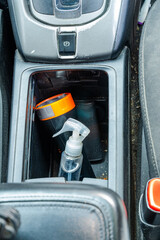 Car console with spray bottle, flashlight, and charger plug beside parking brake button.