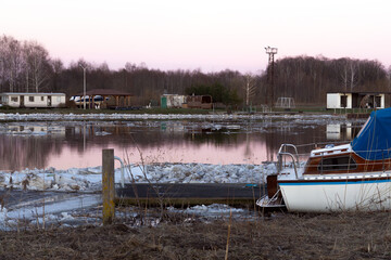 Spring ice drift on river with docked boat and camping site background