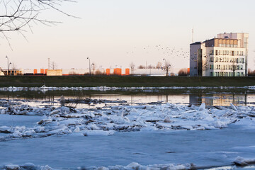 River ice drift landscape with modern building and flying birds at sunset