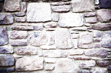 Muro de piedra ajustada con formas irregulares y tonos púrpura, rosa y beige sobre mortero claro.elegancia rústica y ritmo táctil, simbolizando oficio, permanencia y armonía natural.