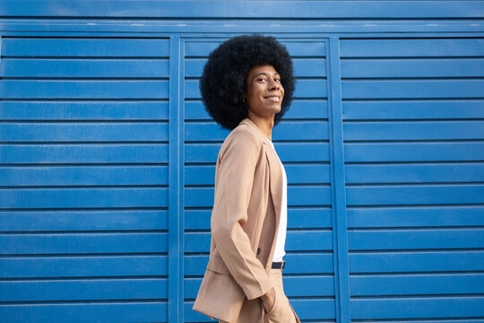 Smiling person in brown blazer against blue backdrop