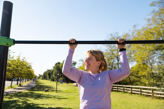 Woman practicing outdoor performs pull-ups on a sunny day