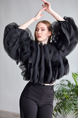 A beautiful woman in a stylish black dress, with long hair and flawless makeup, poses in front of the camera in a professional studio.